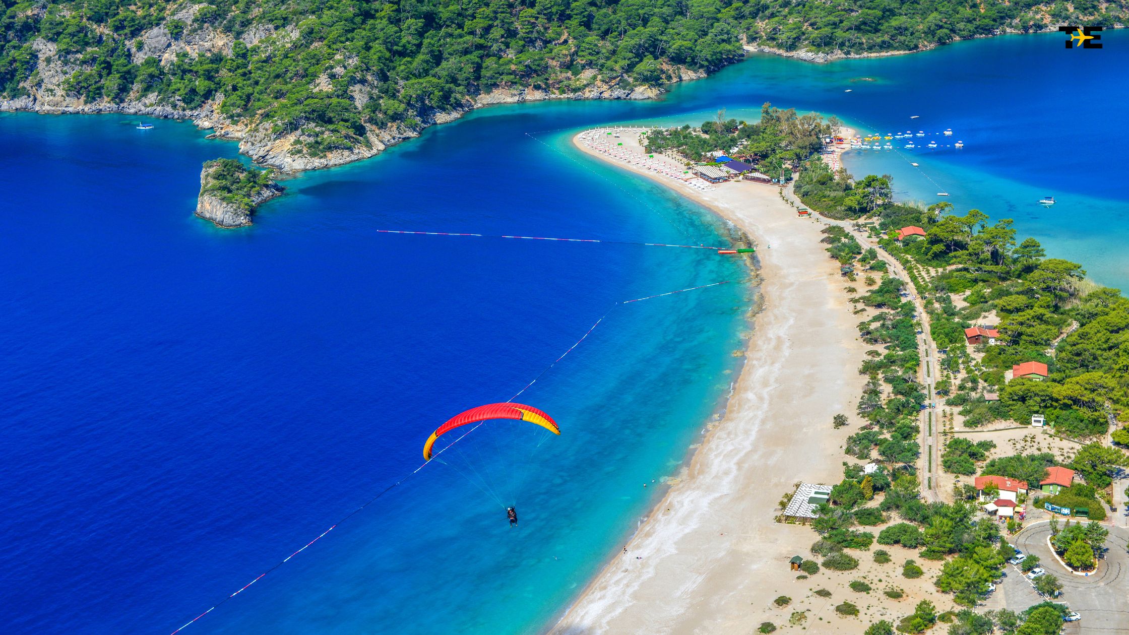 Stunning Fethiye coastal view with paragliding, turquoise waters, sandy beaches, and lush greenery.