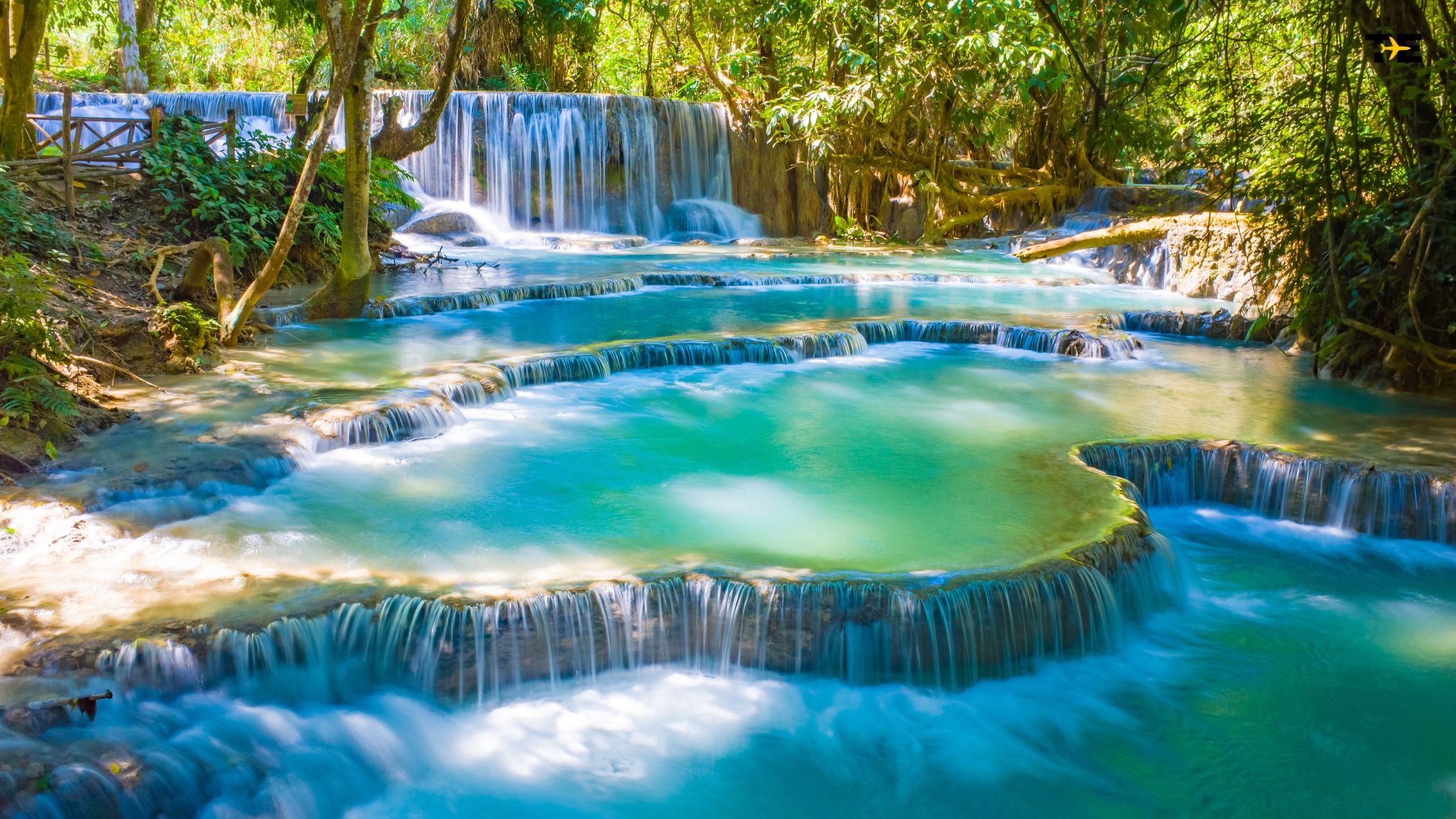 Cascading waterfalls flow into serene turquoise pools, surrounded by lush greenery and vibrant nature.