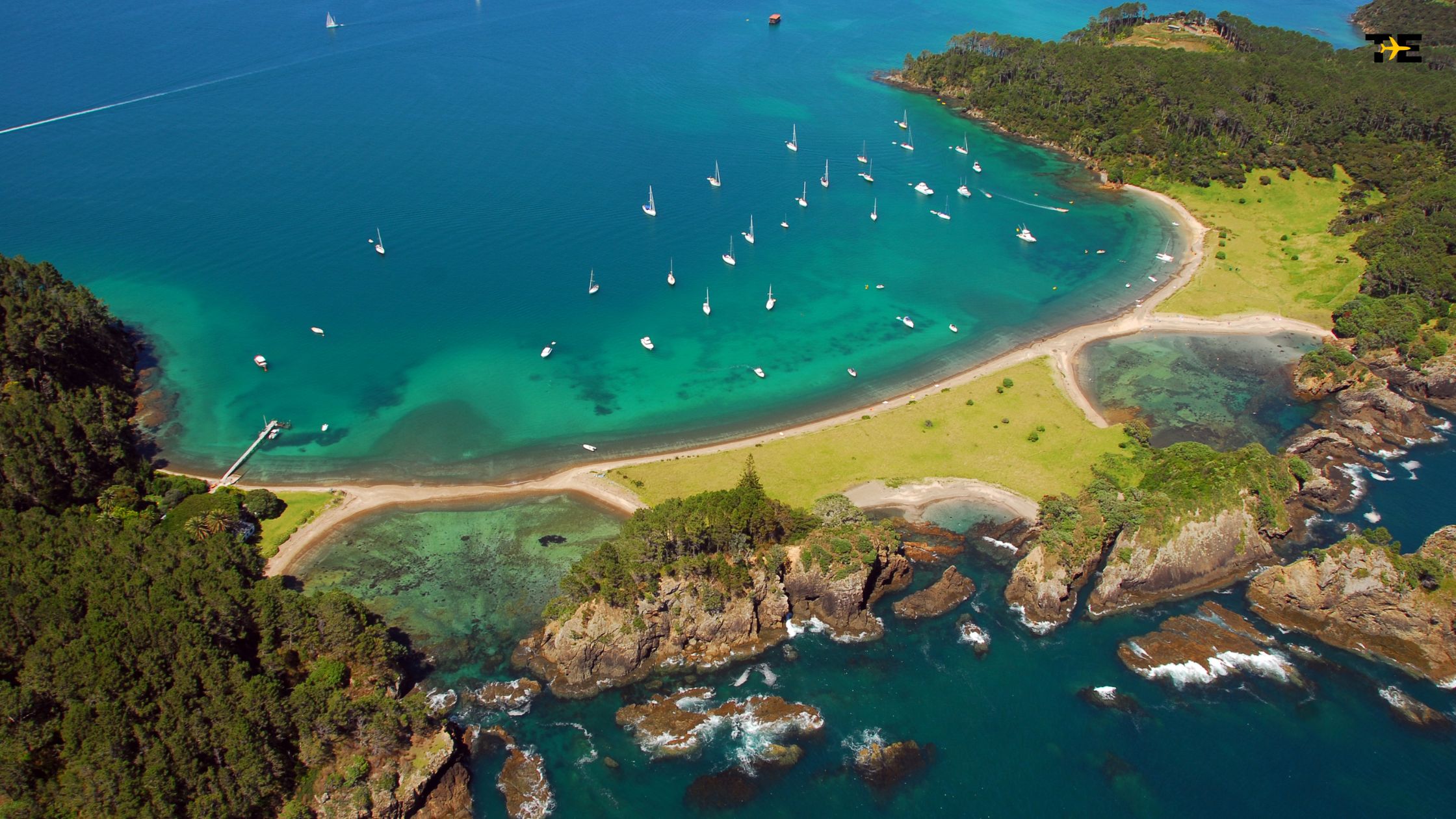 Aerial view of a tranquil coastal bay with turquoise waters, sandy beach, and sailboats.