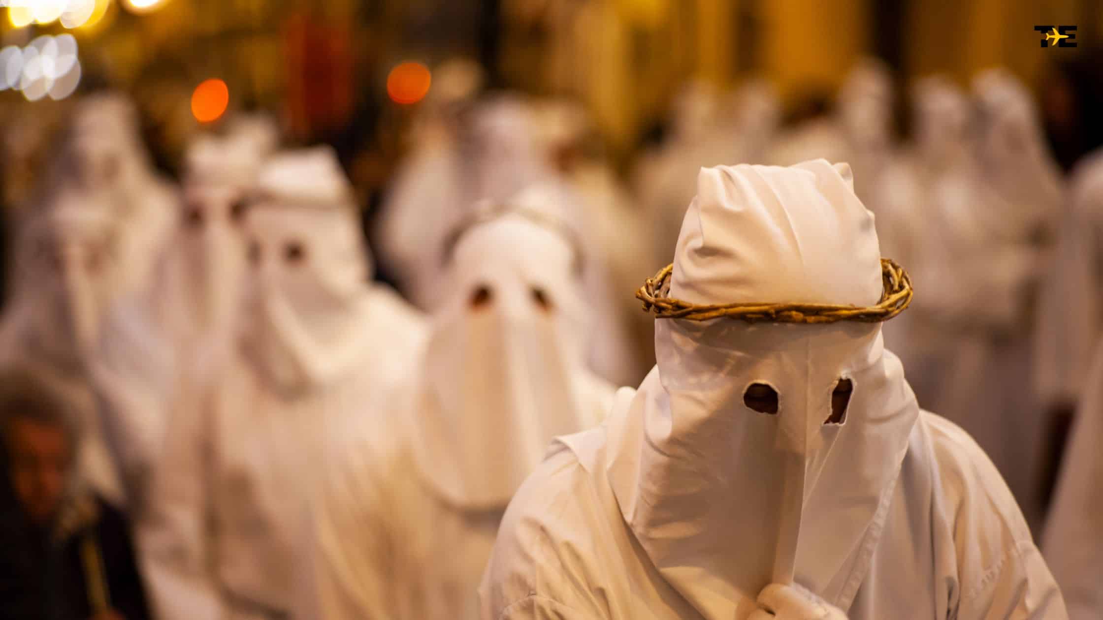 Solemn religious procession with masked figures in white robes and a crown of branches.