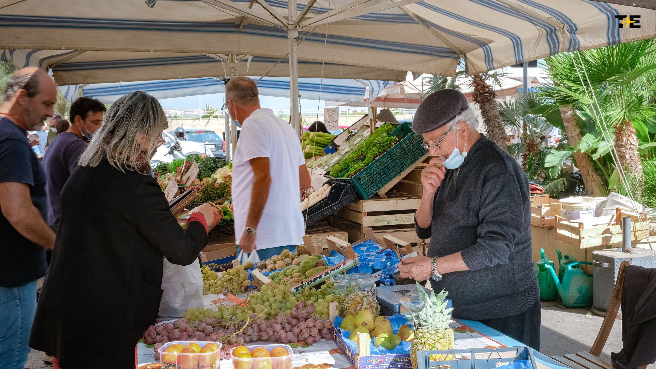 Bustling outdoor market filled with fresh produce, diverse shoppers, and vibrant community interactions.